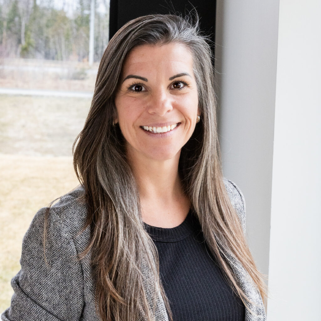 Portrait professionnel d’une employée de Construction RPLH devant une fenêtre, souriante et vêtue d’un veston gris.